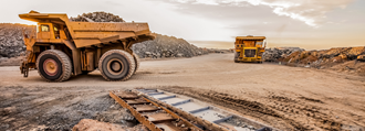 Two large yellow dump trucks transporting minerals at a lithium open mine.